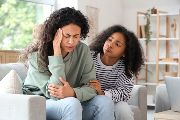 Young African-American woman having headache and her sad daughter at home