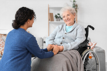 Young African-American female medical worker with elderly woman on wheelchair in nursing home