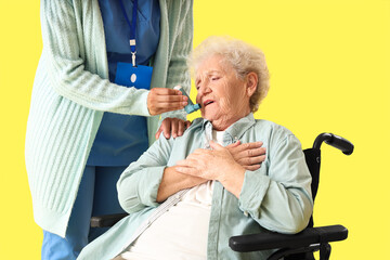 Young African-American female medical worker giving inhaler elderly woman on wheelchair against...