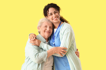 Young African-American female medical worker with elderly woman against yellow background