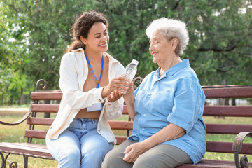 Young African-American female medical worker giving bottle of water to elderly woman outdoors