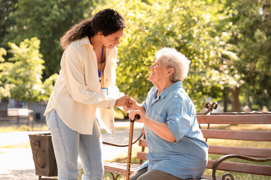 Young African-American female medical worker helping elderly woman outdoors