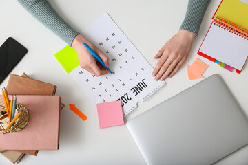 Young woman with laptop marking date in calendar at workplace, top view