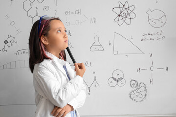 Thoughtful little girl near whiteboard at chemistry lesson in classroom