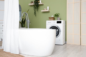 Bathtub with curtain and washing machine in interior of modern bathroom