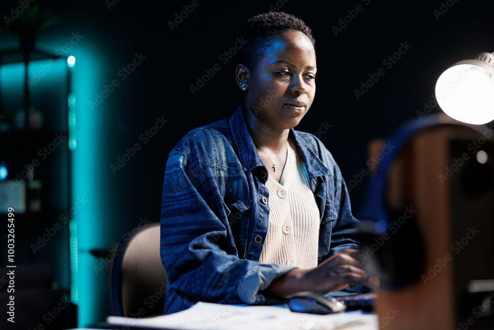 Poster dedicated african american woman working from a modern apartment. focused and using her laptop to br