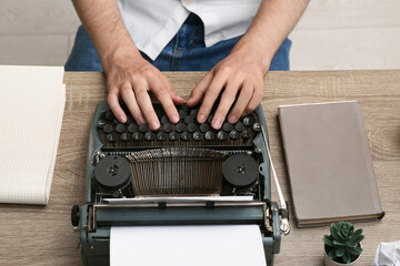 Young writer with vintage typewriter typing at table in room, closeup