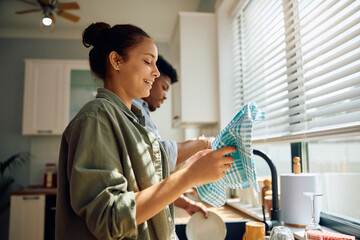 Happy Hispanic woman and her boyfriend doing dishes in  kitchen.