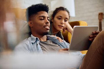 Young couple using digital tablet while relaxing at home.