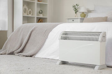 Electric heater on floor near bed in bedroom, closeup