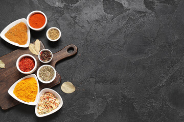 Composition with bowls of various aromatic spices and wooden board on dark background