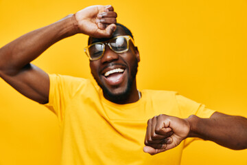 Happy man dancing joyfully in yellow outfit and sunglasses, expressing fun and energy against a...