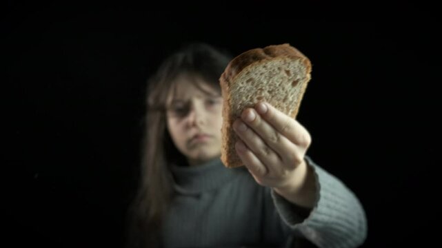 Girl takes food from volunteer. A child during poverty ask for bread against black background.