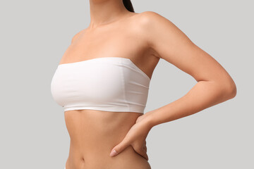 Young woman in bandeau top with beautiful breasts on grey background, closeup