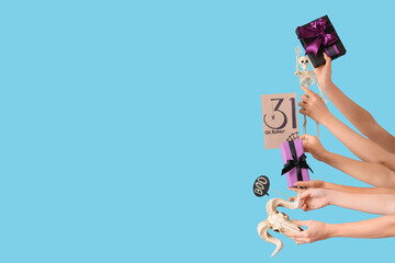 Female hands with Halloween gifts, card, skeleton and skull on blue background
