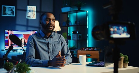 Fototapeta premium Smiling influencer in cozy home using professional camera to film live broadcast for online streaming platforms. Internet star hosts q a session with audience members using recording equipment
