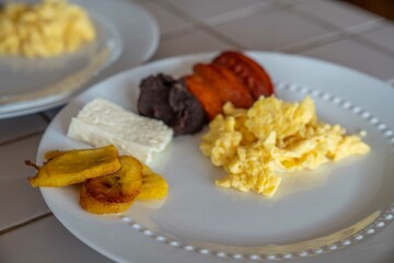 close up of breakfast platter with plantains, eggs, chorizo, cheese, and refried beans