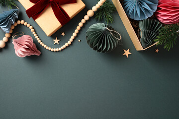 Scandinavian paper honeycomb Christmas ornaments in the box, craft paper gift box, wooden garland on pastel green background. Elegant modern Xmas decorations. Flat lay, top view.