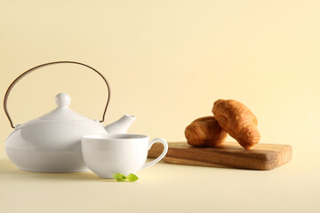 Beautiful composition with tea pot, cup and croissants on beige background