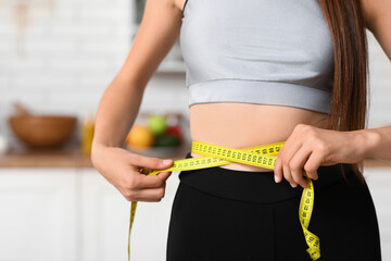 Sporty young woman measuring her waist in kitchen, closeup. Diet concept