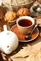 Teapot with cup of hot beverage, tasty cupcakes and autumn leaves on windowsill