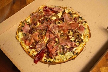 large thin crust pizza pie covered in delicious ham, cheese, and sauce in to go box