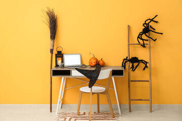 Workplace with laptop, pumpkins and broom in comfortable office interior decorated for Halloween celebration
