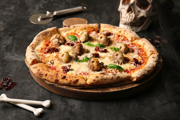 Wooden board of tasty pizza with mushrooms and skull for Halloween celebration on black background