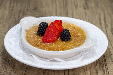 Creme brulee dessert is served sweet with sliced strawberry and blackberry on top