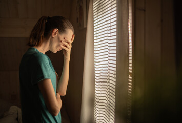 Sad woman in a dark room full of desperation thoughts. Portrait of thoughtful sad female alone. Fear, sadness, abuse, depression, addiction.