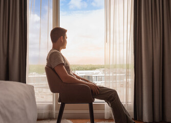 Thoughtful happy relaxed content man at home looking out his window at the view 