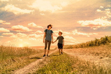 Happy smiling mother and child holding hands walking in the countryside