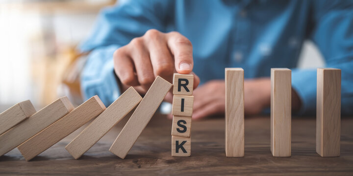 A person is putting a block on top of a stack of blocks that spell out the word RISK
