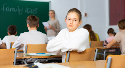 Teen girl listening to lecturer and writing in notebook in classroom