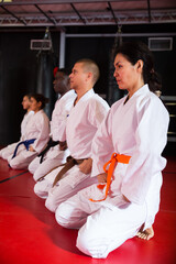 Group of multiracial people in kimono kneeling on floor during karate training. © JackF