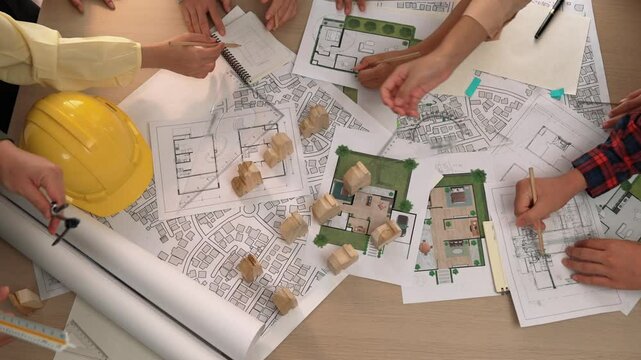 Architect and safety engineer discussion about building construction use blueprint on table with architectural document, measurement tool and wooden block scatter around at modern office. Delineation.