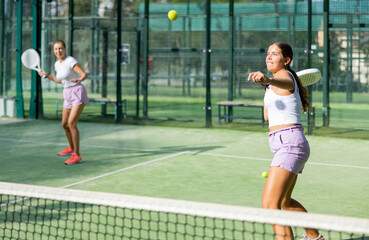 Obraz premium Two young active women tennis players with rackets playing padel on an outdoor court