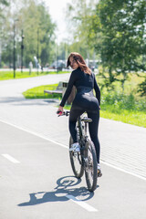 Fototapeta premium Rear view of Caucasian woman riding bike in park. Vertical photo. 