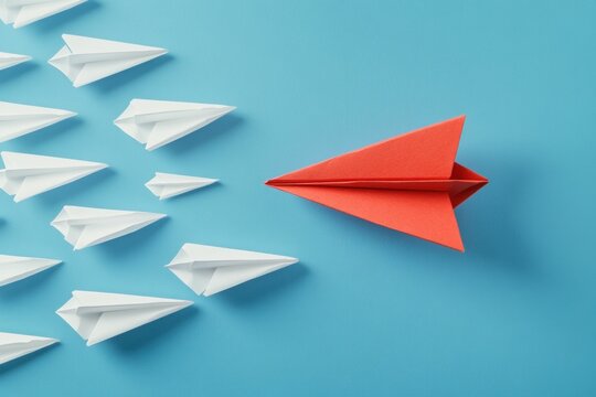 paper airplanes, creativity, leadership, innovation, teamwork, competition, motivation A striking image featuring a bold red paper airplane leading a group of white ones against a vibrant blue backg