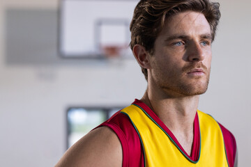 Wearing basketball jersey, man standing in gym, looking determined and focused, copy space