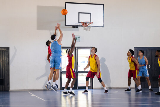 Playing basketball, athletes jumping to shoot ball while others defend in gym