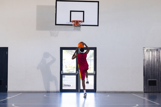 Playing basketball, man jumping and shooting ball towards hoop in gymnasium