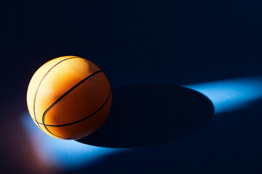 Basketball resting on court under dramatic lighting and shadow, copy space