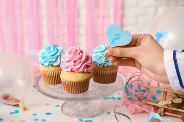 Female hand with delicious cupcakes and decorations on table against white brick background. Gender reveal party concept
