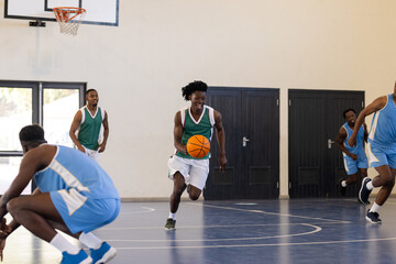 Playing basketball, man dribbling ball on indoor court with teammates