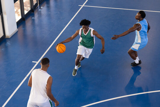 Playing basketball, three African American men in action on indoor court, dribbling and defending