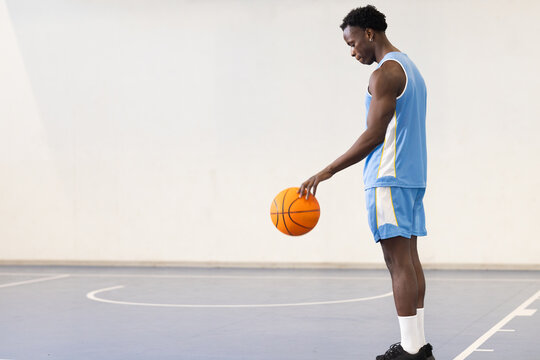 Dribbling basketball, athlete in blue uniform practicing on indoor court, copy space