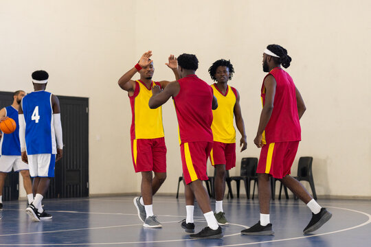 Playing basketball in school gym, team celebrating successful play, wearing uniforms