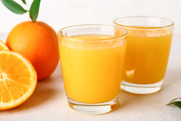 Glasses of fresh orange juice and leaves on white background