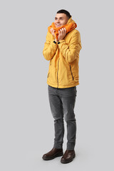 Young man in yellow stylish jacket and scarf on grey background